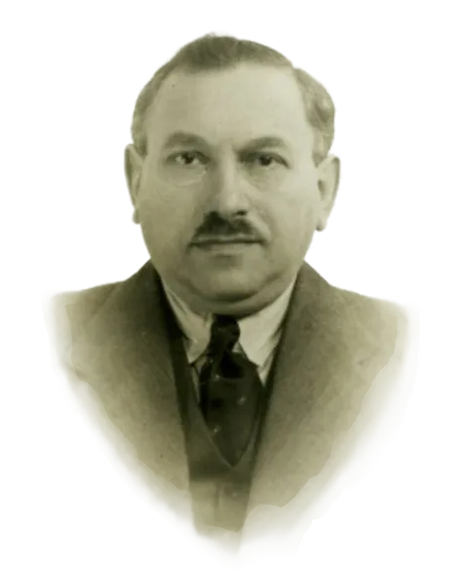 A formal, close-up portrait of Rodi’s grandfather. He has short, thinning hair and a neat mustache. He is dressed formally in a dark suit jacket, a matching vest, and a dark patterned necktie over a white collared shirt. 
