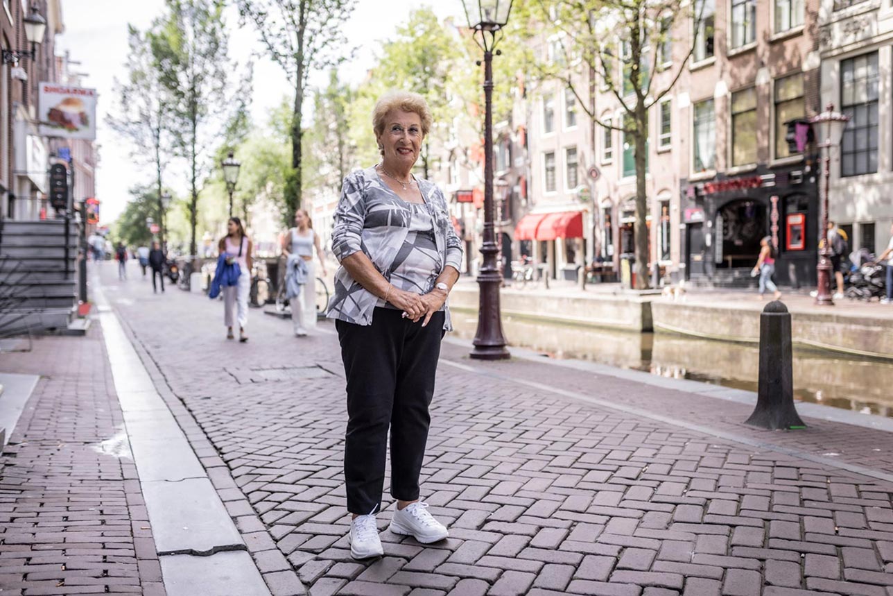 Close-up contemporary portrait of Rodi standing on a brick-paved street beside a canal in Amsterdam.